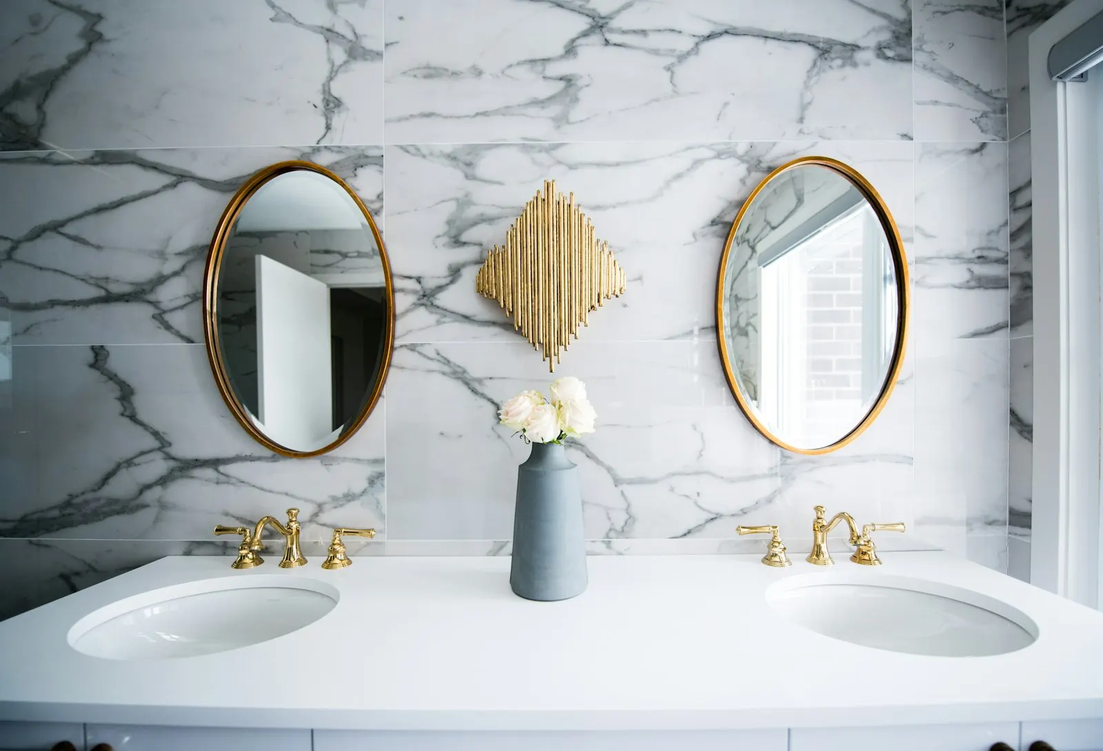 Marble-clad bathroom with two sinks, brass faucets and oval brass mirrors