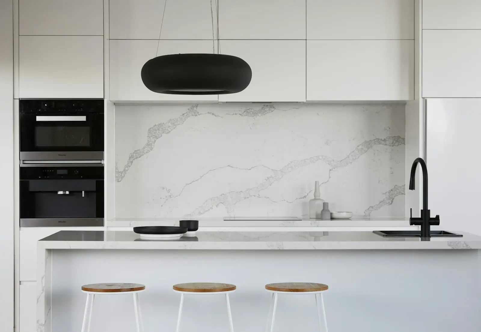 Modern white kitchen with a marble backsplash and built-in ovens