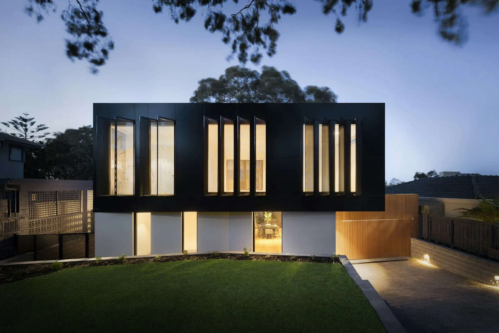 Dark-clad modern home with tall lit windows at dusk