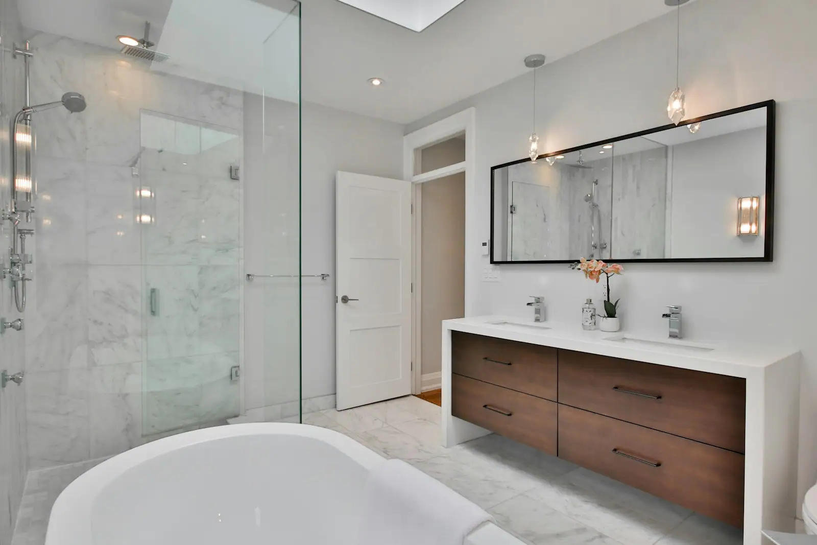 Walnut double vanity beside a glass shower and soaking tub